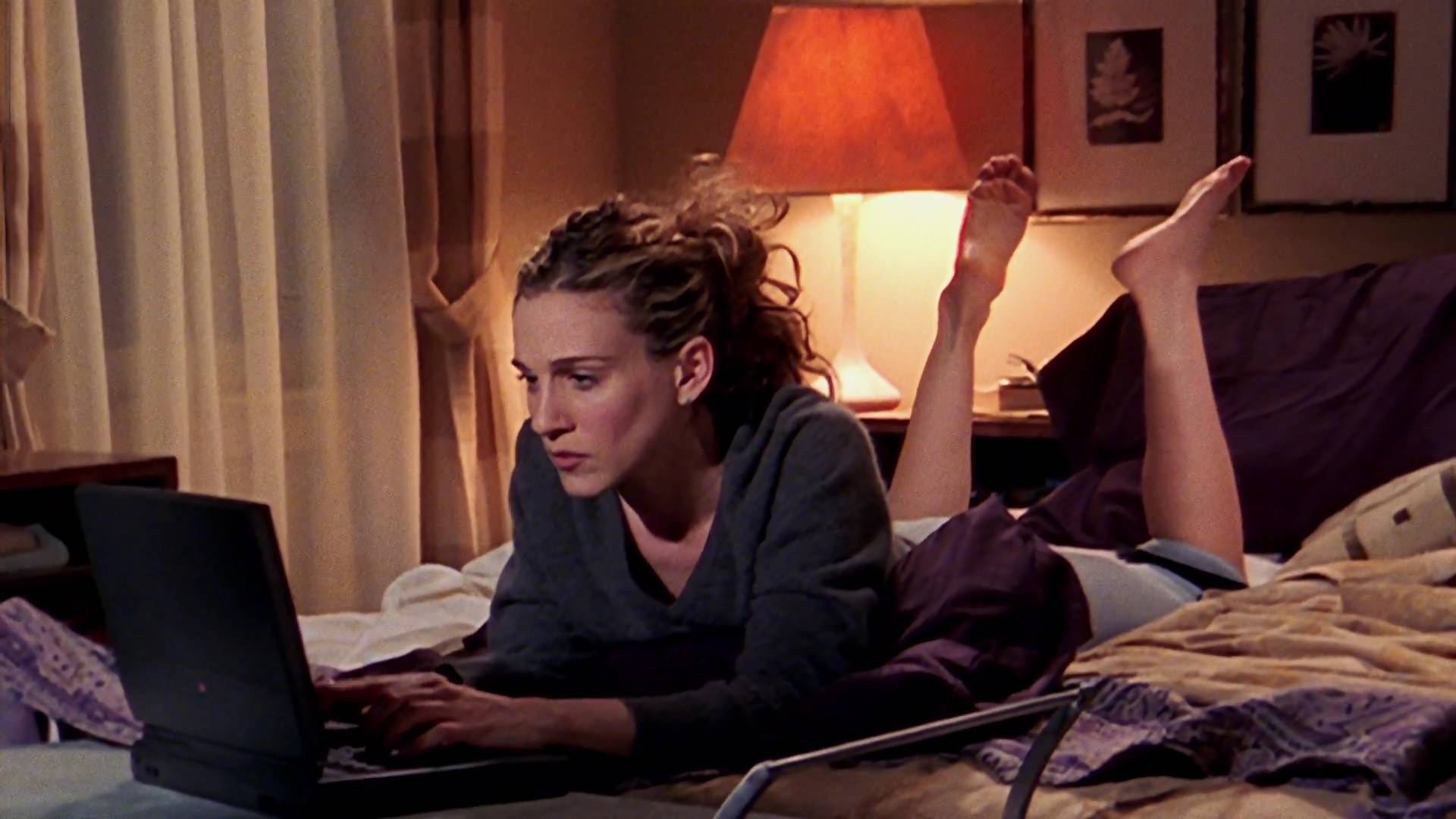 A woman working on a laptop while lying on a bed